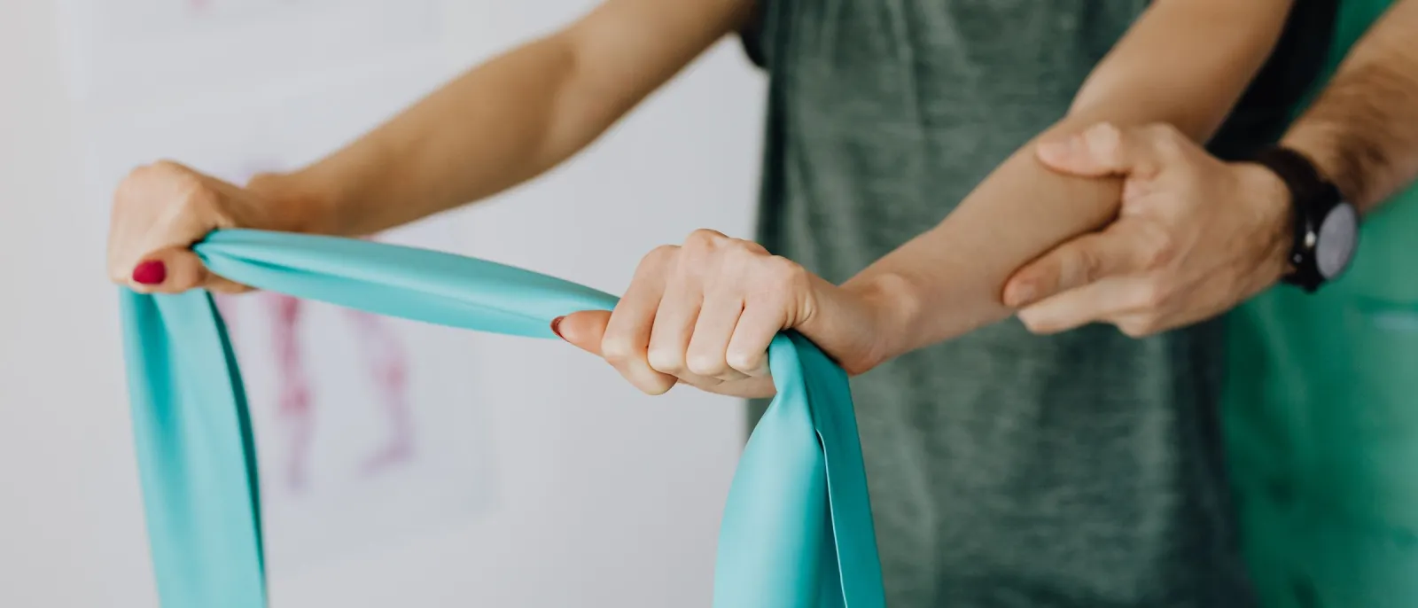 Close-up of hands stretching a teal resistance band while a therapist supports the patient's arm