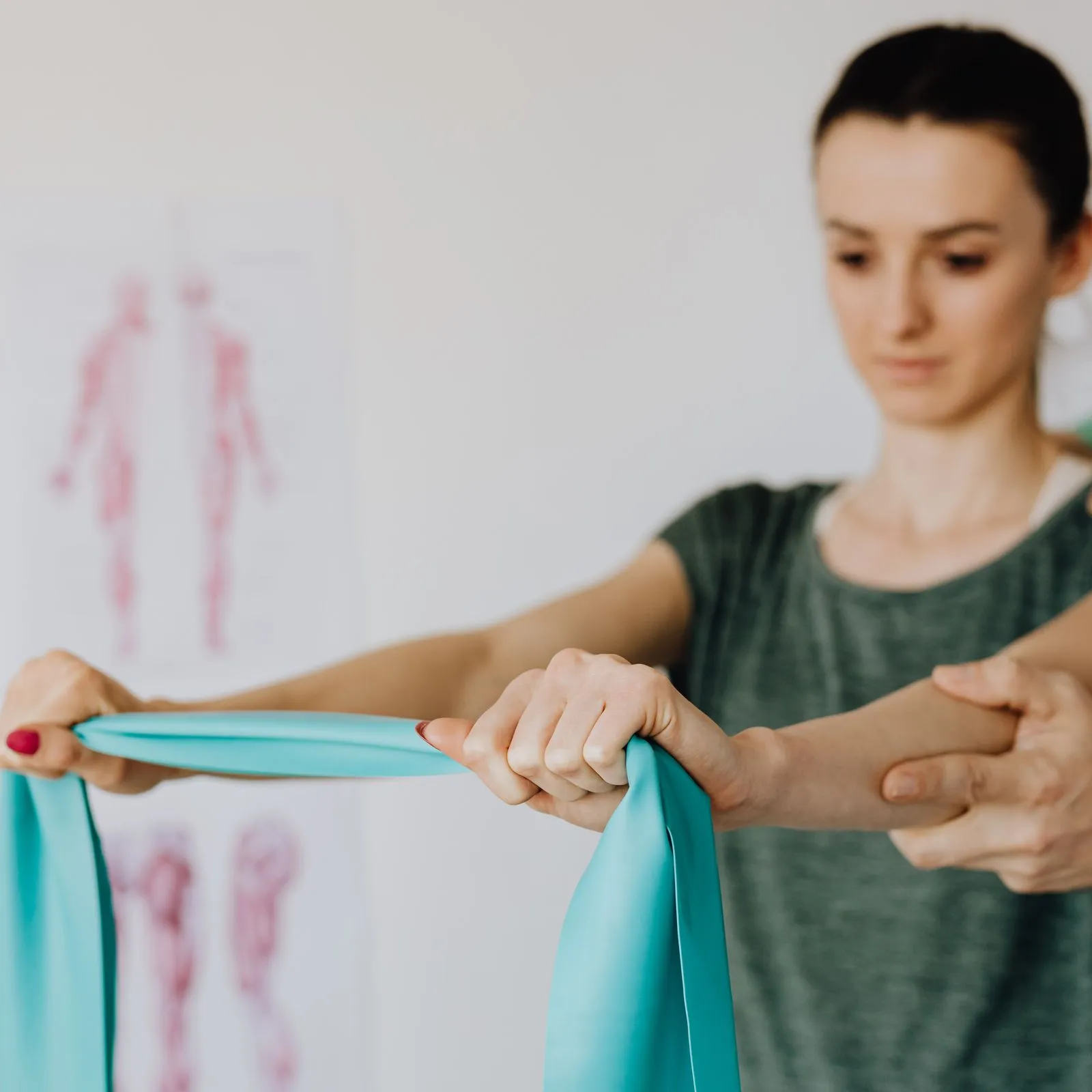 Physiotherapist guiding a patient's arms as she stretches a teal resistance band in a bright clinic