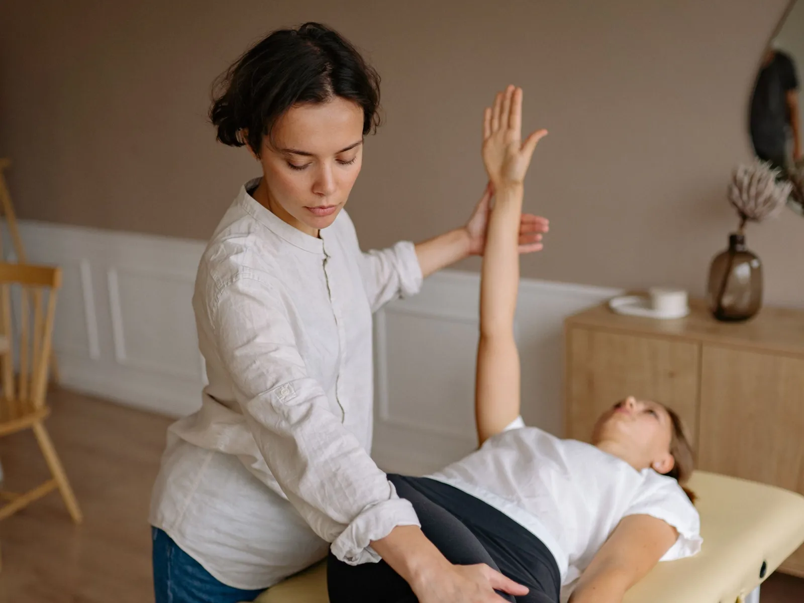 Physiotherapist supporting a patient's raised arm and hip on a treatment table in a warm-toned studio