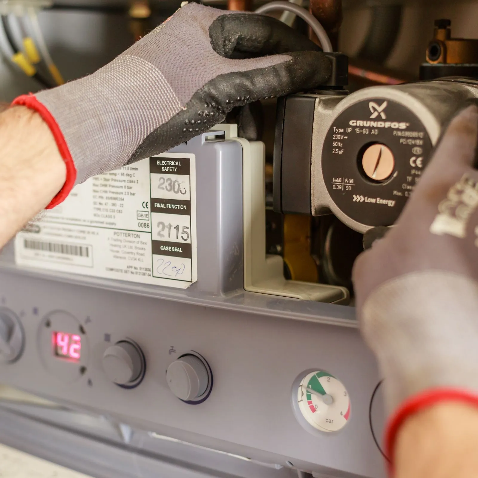 Gloved hands adjusting the circulation pump inside an open combi boiler during a service
