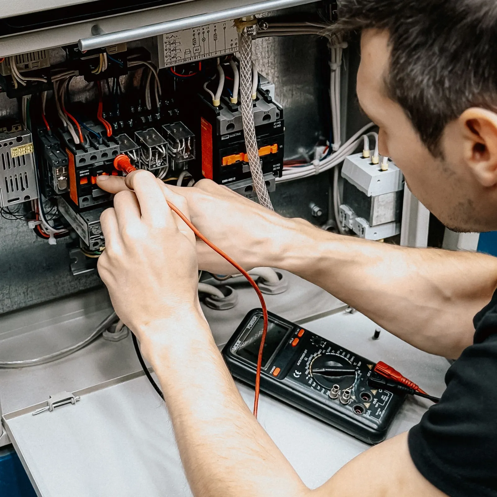 Technician probing an open control cabinet with multimeter leads during an electrical check