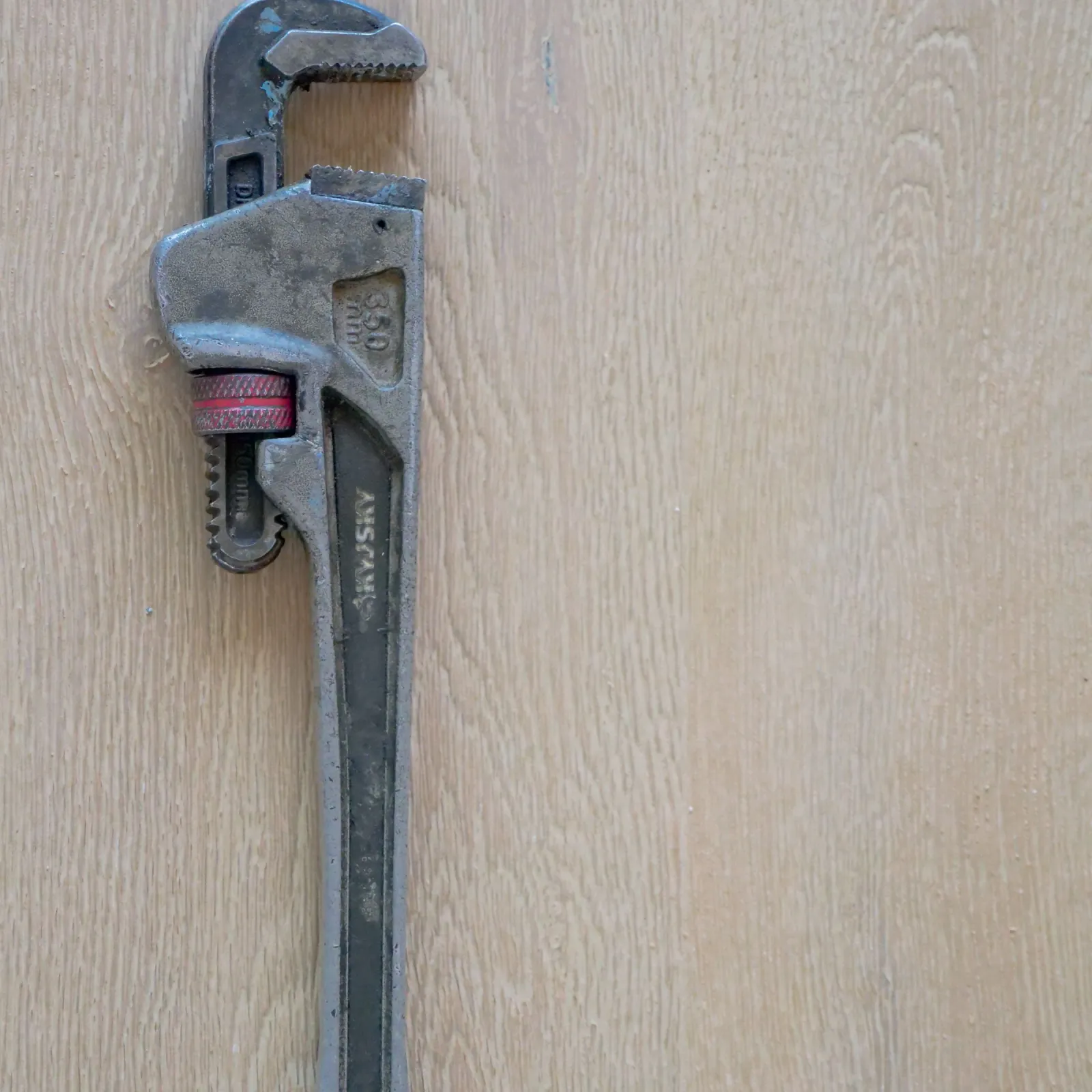 Weathered pipe wrench with a red adjuster ring resting on pale oak boards