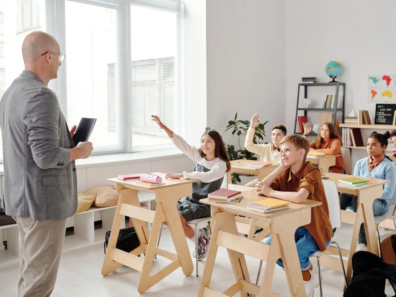 Students raising their hands while a teacher leads a lesson in a bright classroom