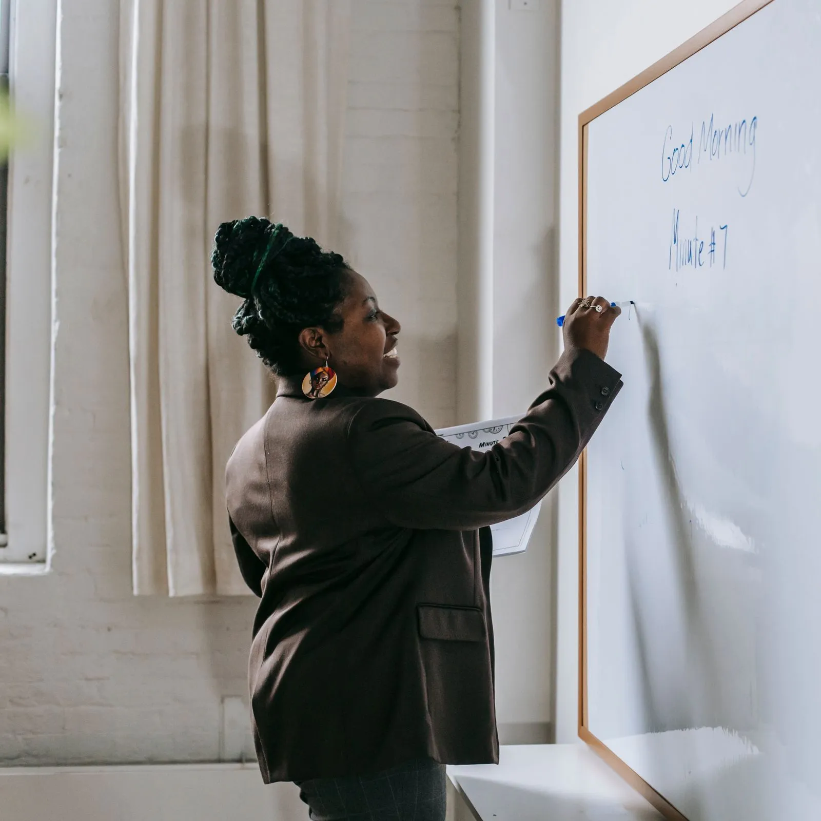 Tutor writing a greeting on a large whiteboard in a naturally lit room