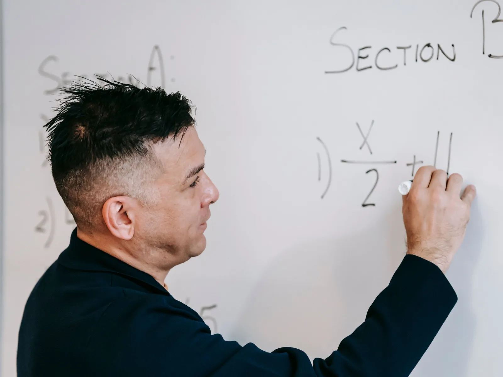 Male tutor writing algebra equations on a whiteboard with a marker