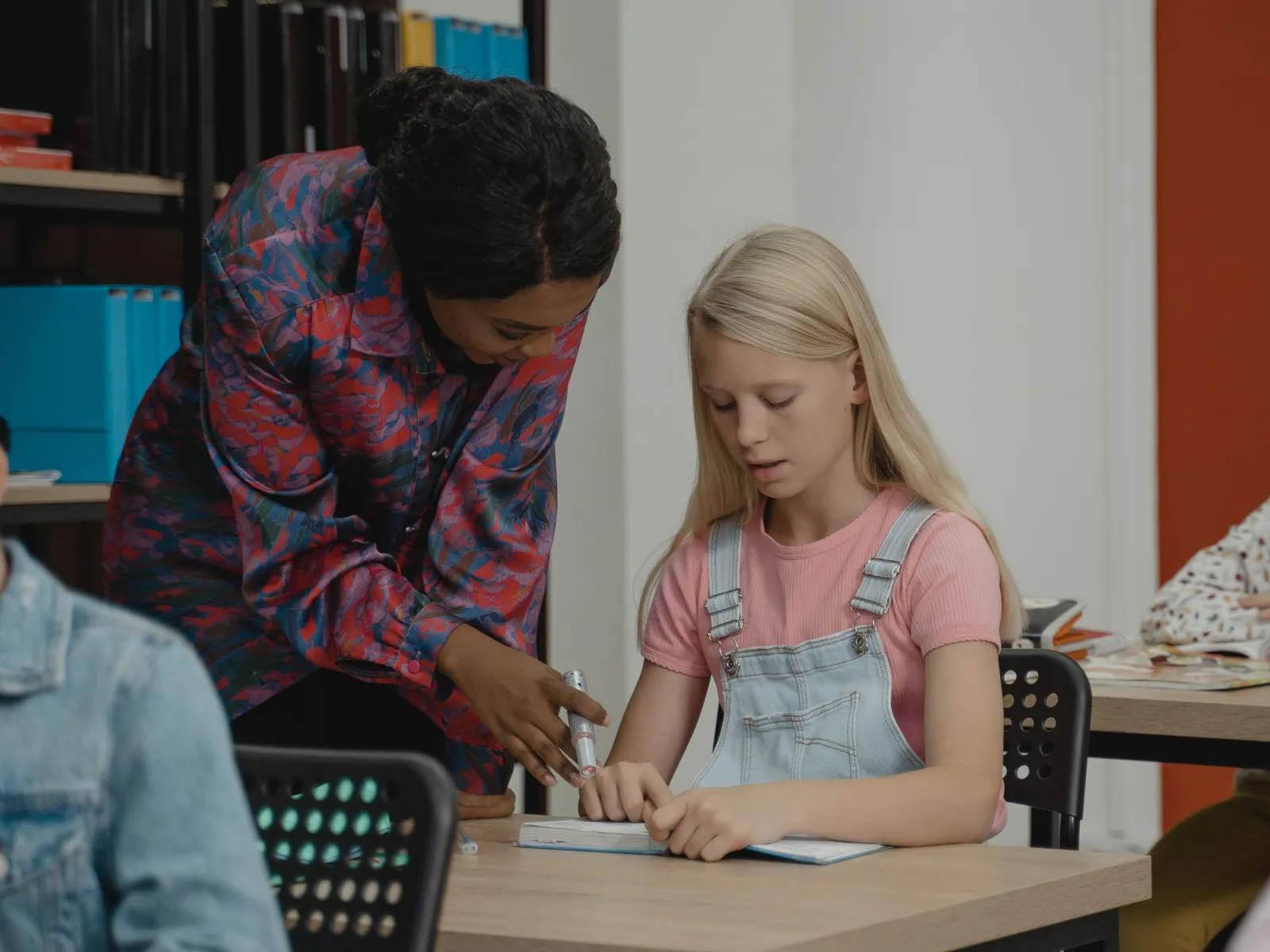 Tutor leaning over a desk to help a young student with her workbook